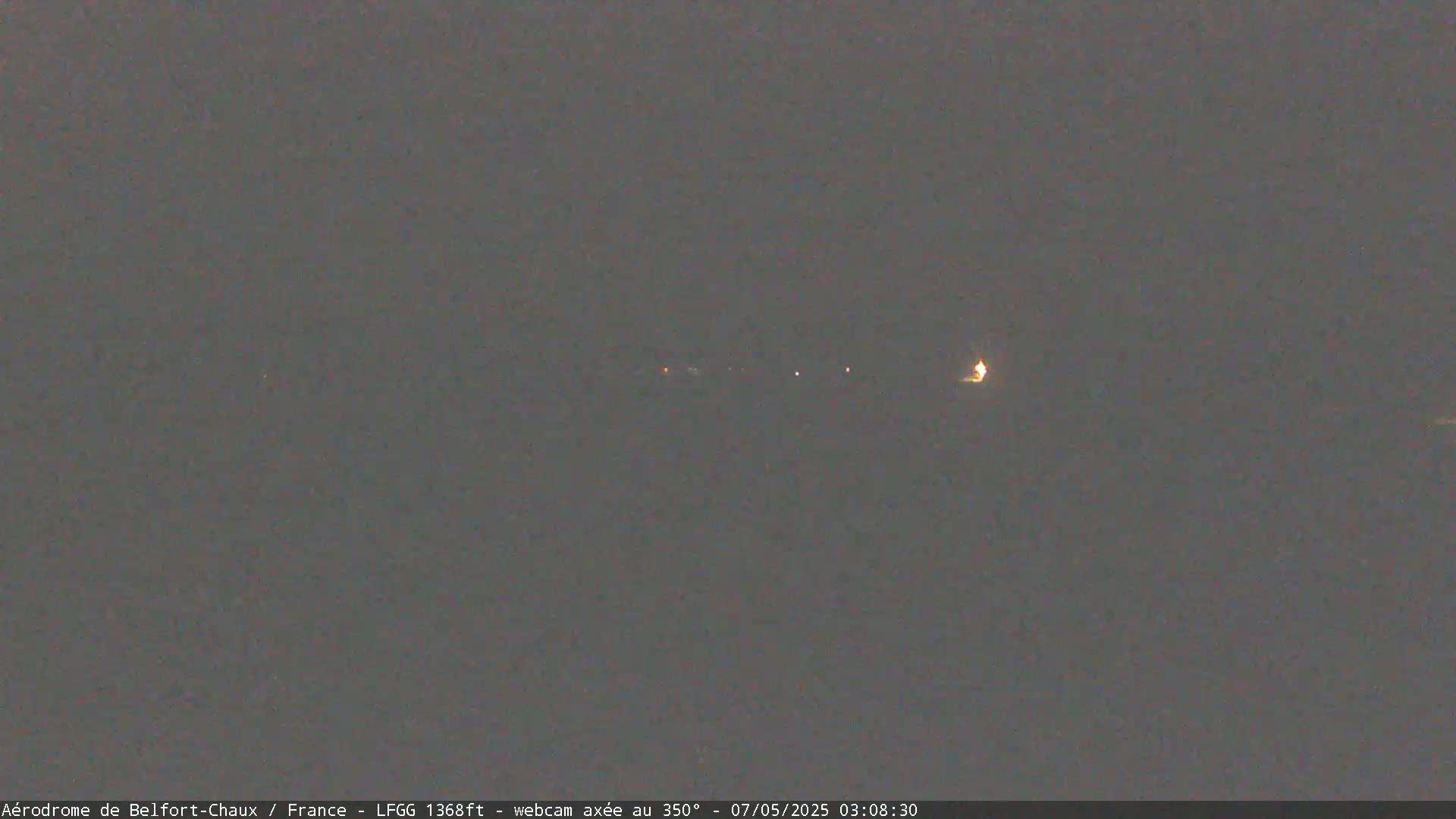 A dark, nighttime scene shows a few faint lights in the distance under a gray sky.