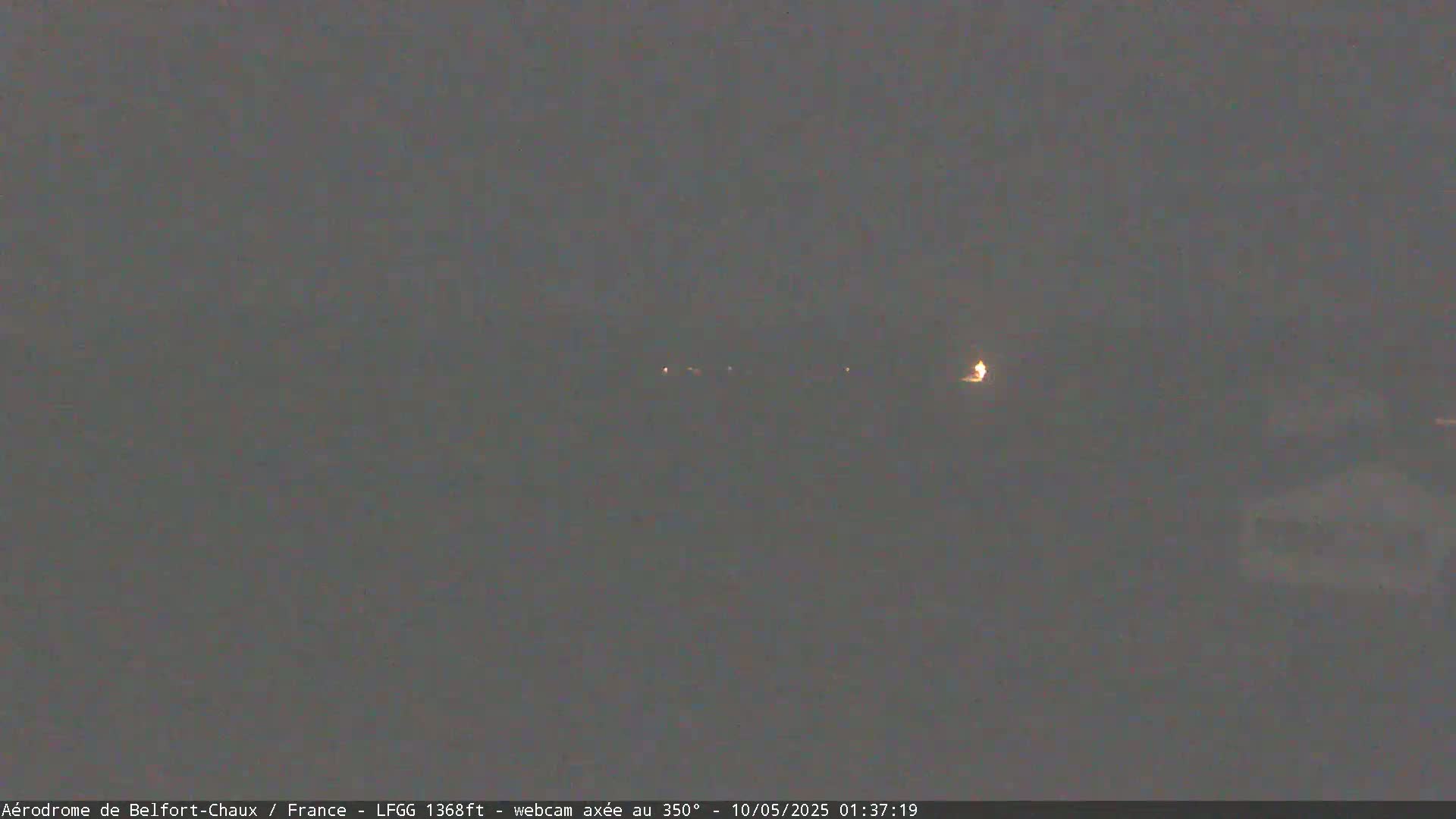 A dimly lit, nighttime scene shows a few distant lights in a dark, overcast landscape.