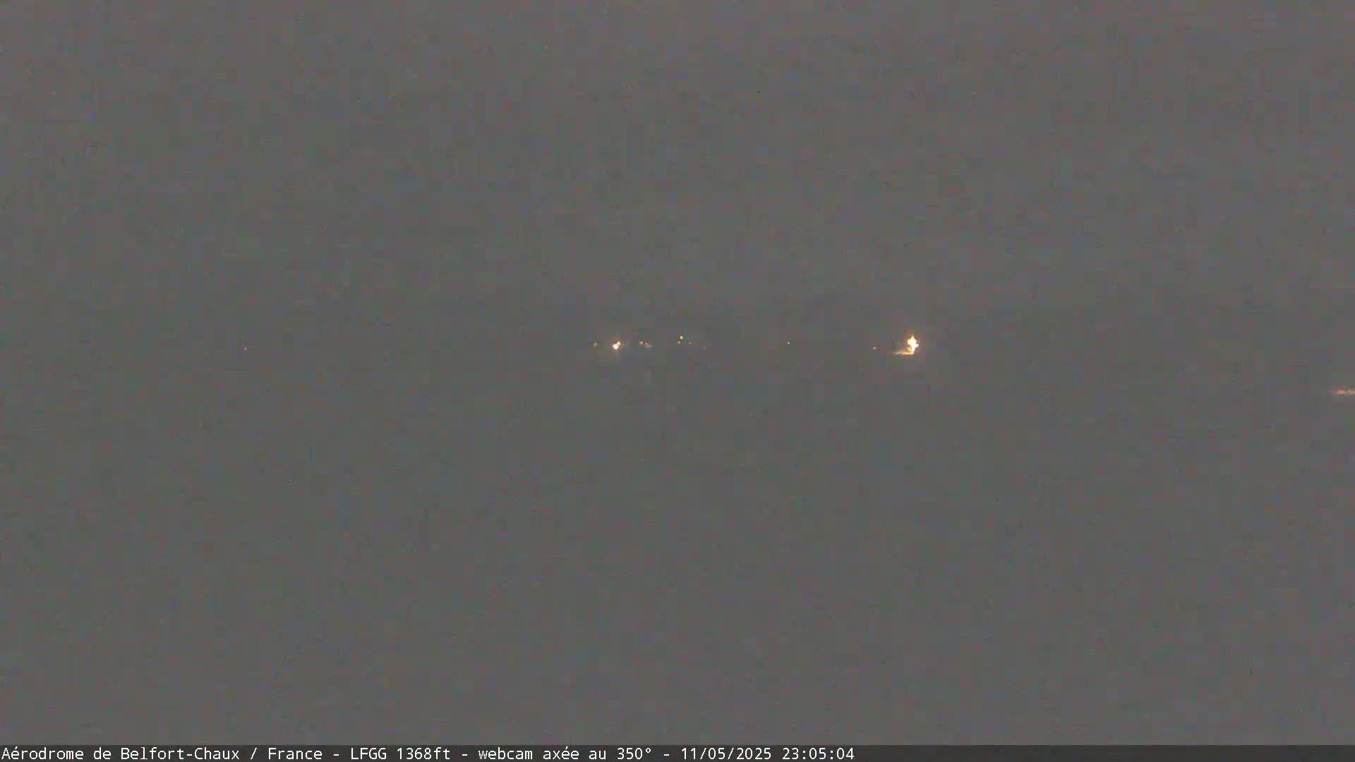 A dark, nighttime scene shows a few distant lights in the hazy distance.