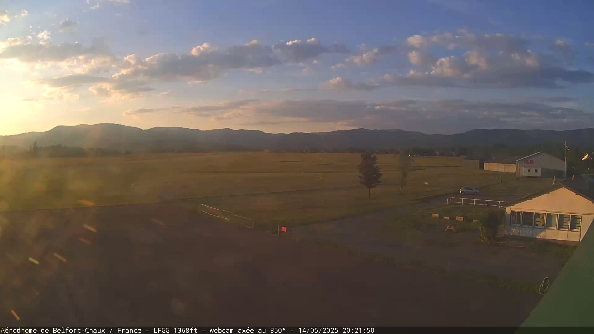 A wide, flat field stretches towards distant mountains under a partly cloudy sunset sky.