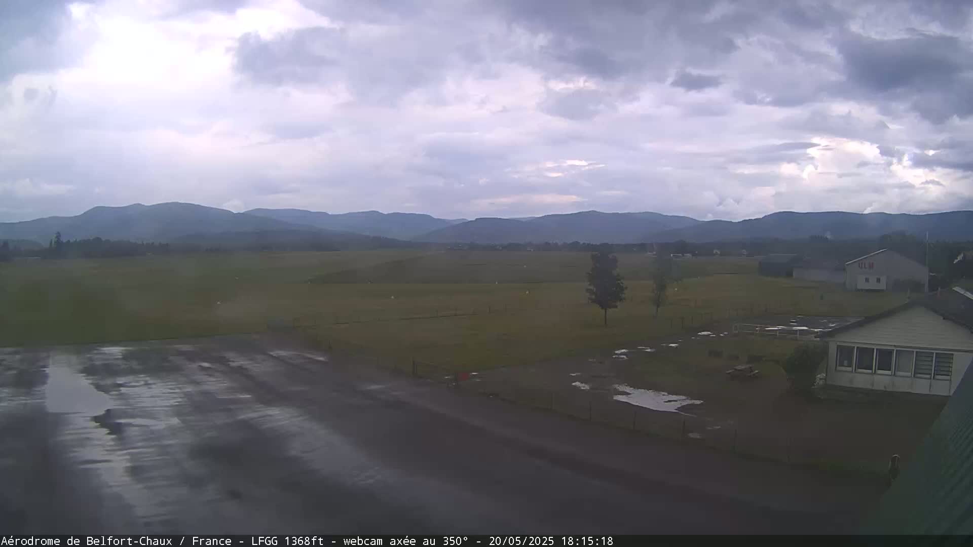 A wet airfield with a small building and distant mountains under an overcast sky.