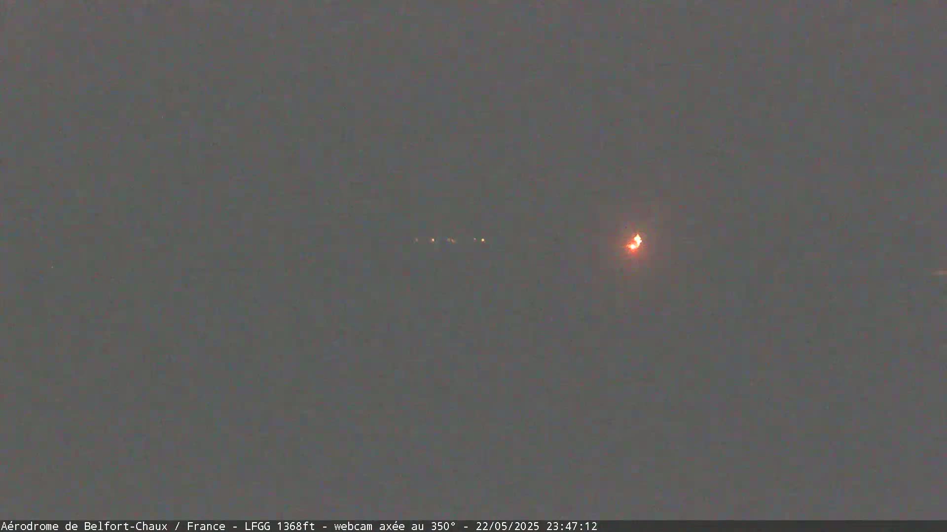 A nighttime, dimly lit scene shows a distant orange light and several fainter lights in the dark sky.