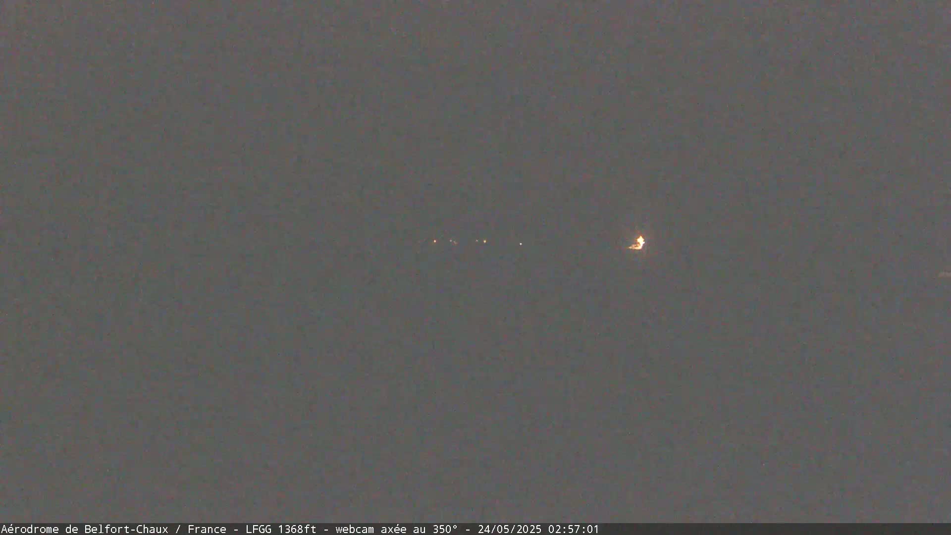A dark, nighttime scene shows a line of faint lights in the distance.