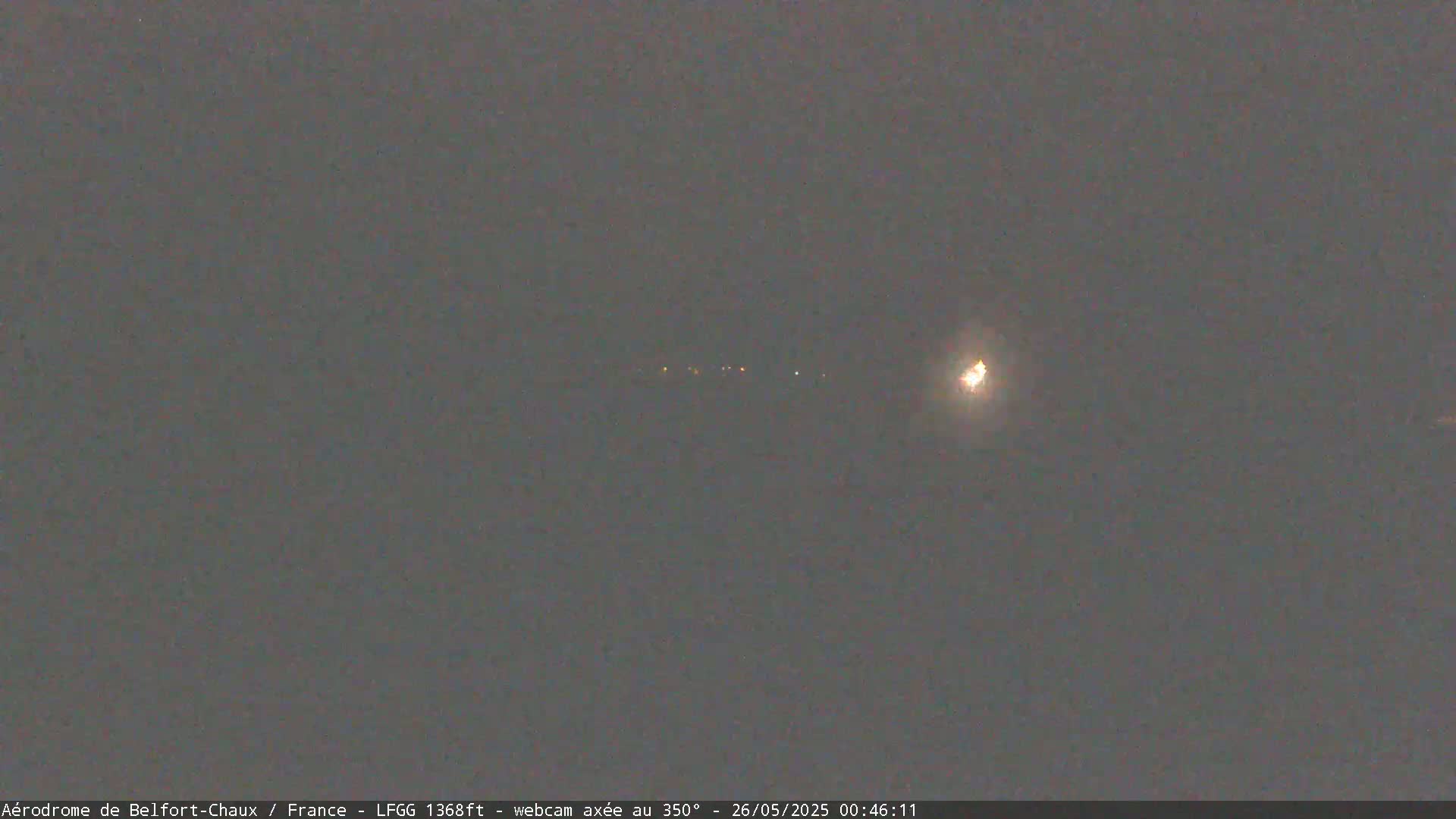 A nighttime long shot shows a bright light in the distance with a few fainter lights below it, in a dark, overcast sky.