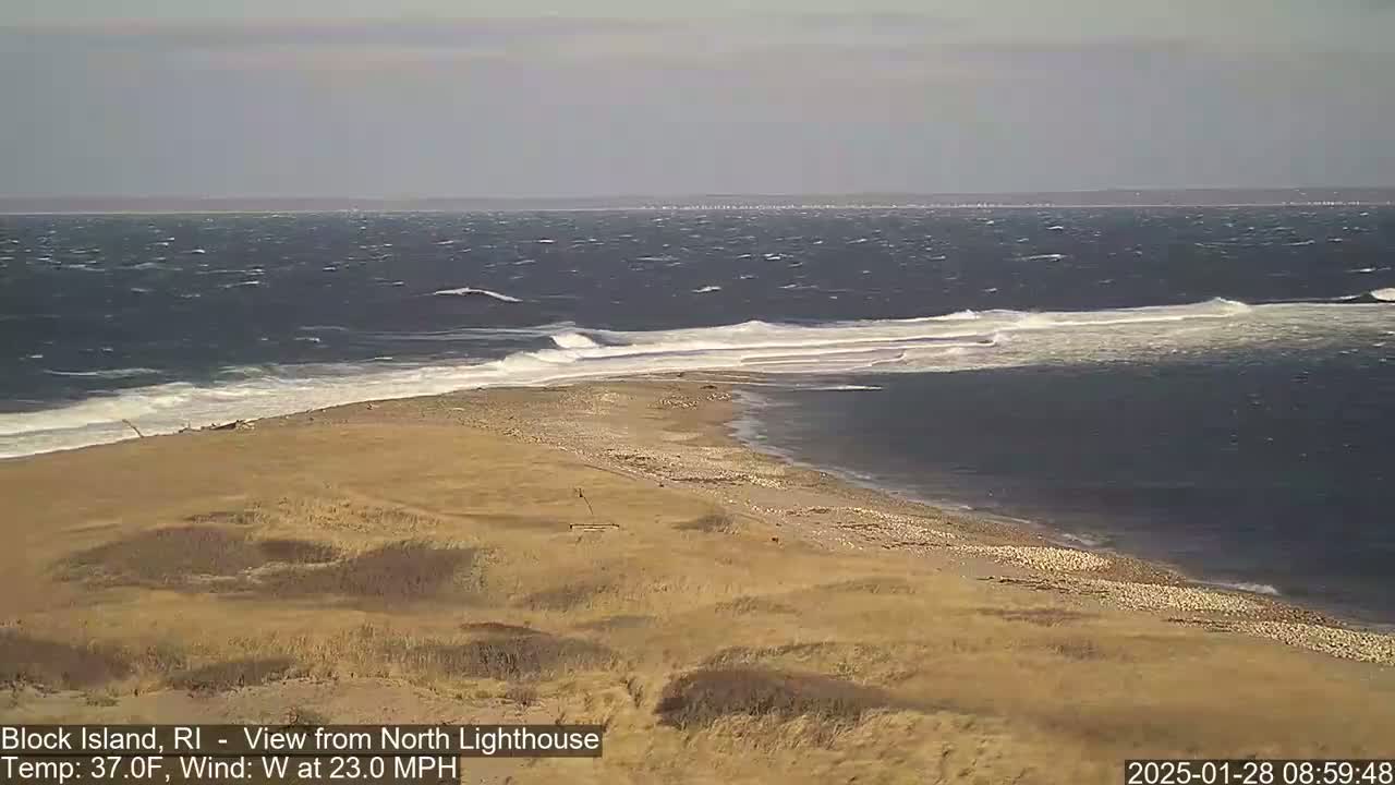 A sandy beach with dry dune grass slopes down to a windy ocean with moderate waves.