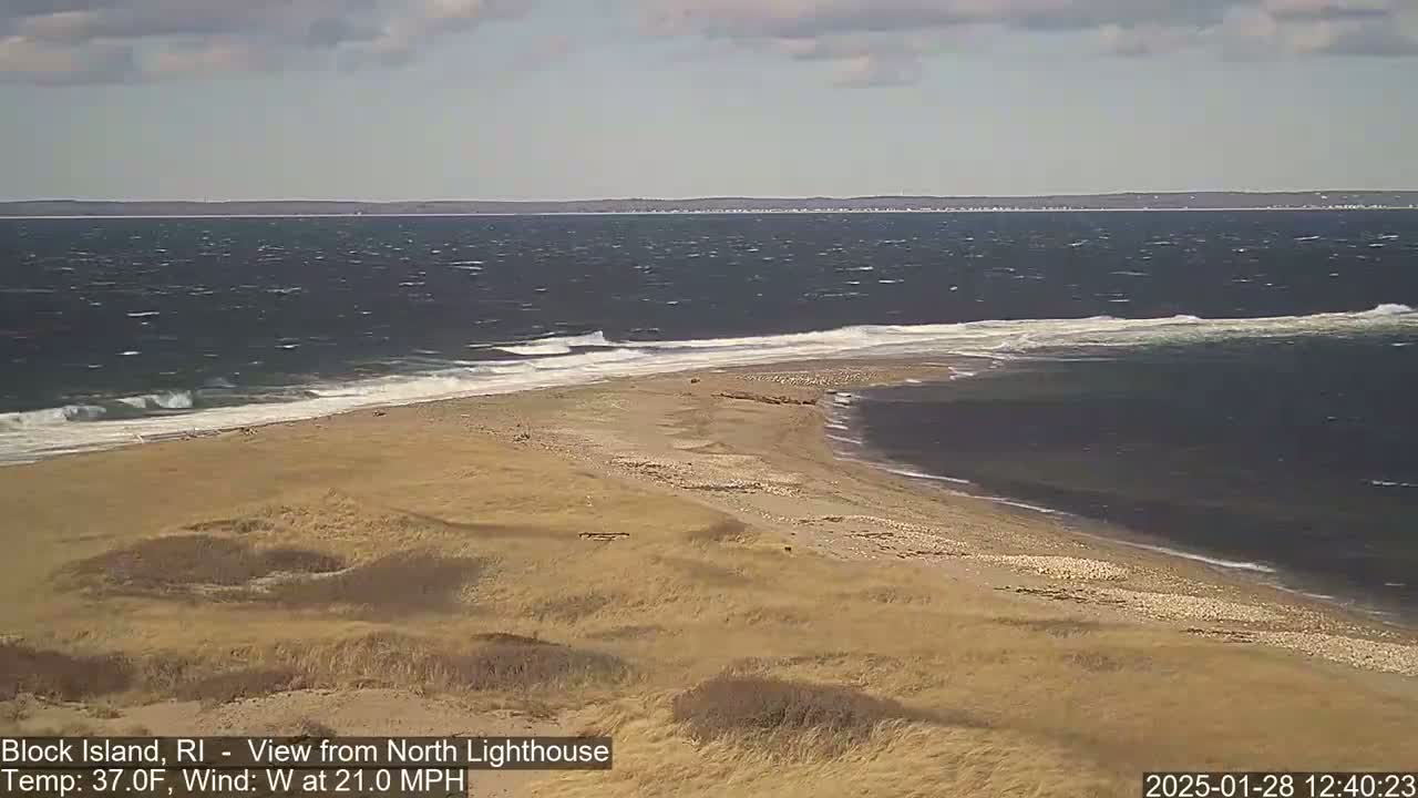 A windy, sandy beach with choppy waves crashes on the shore under a partly cloudy sky.