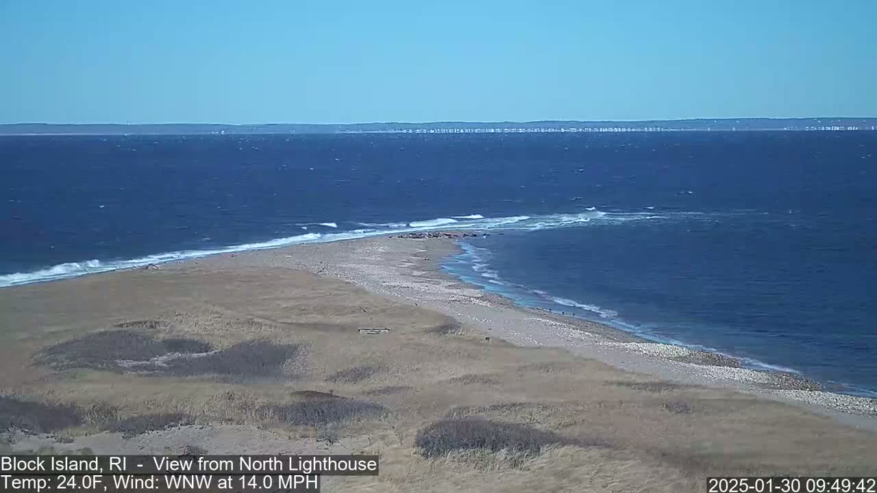 A sandy beach and a point of land jutting into a blue ocean with small waves under a clear sky.