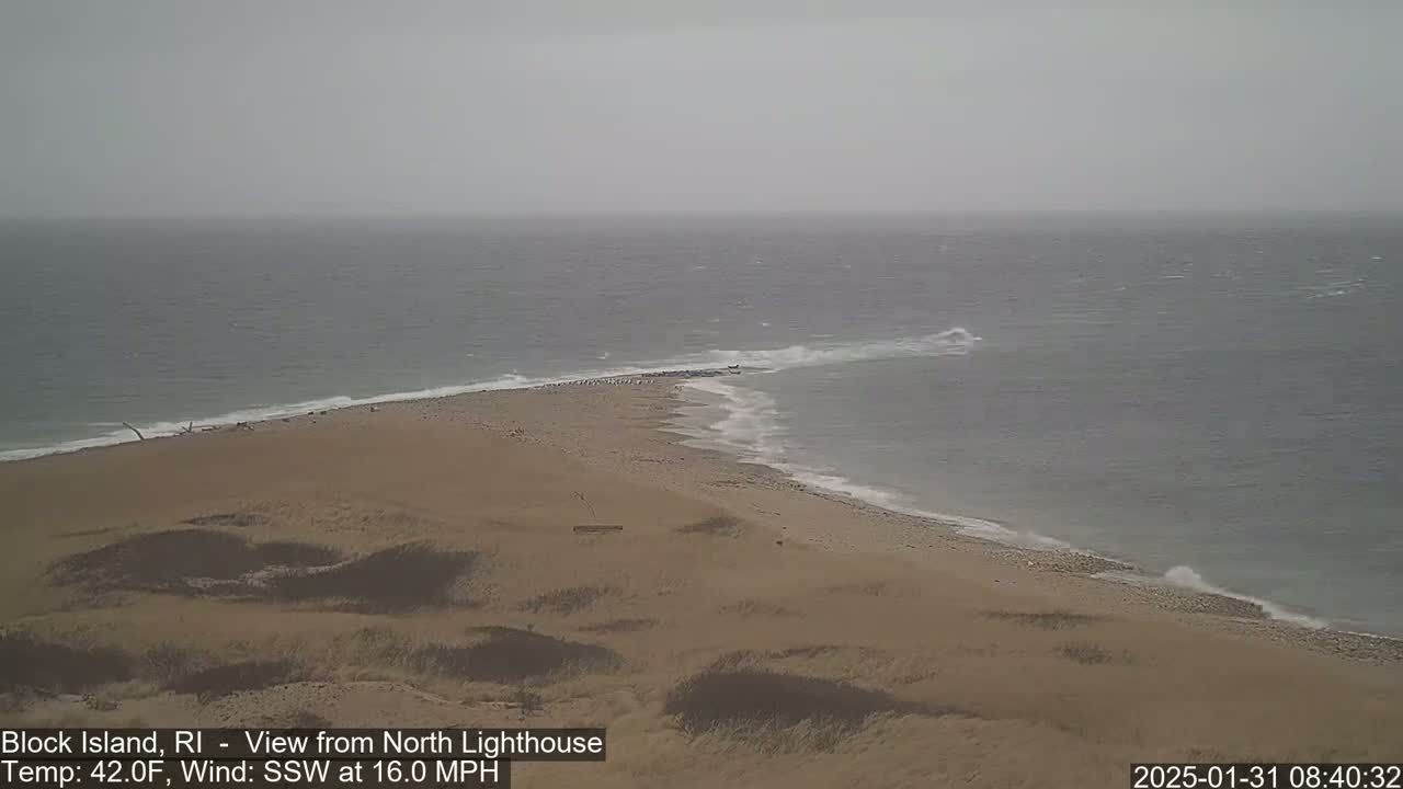 A sandy beach and a gray, windy ocean meet at a narrow spit of land under an overcast sky.