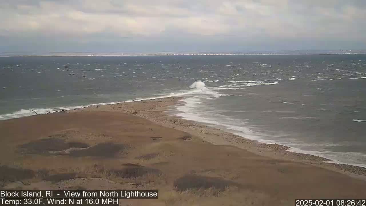 A windy, gray day at the beach shows waves crashing on a sandy shore with a land spit extending into the water.