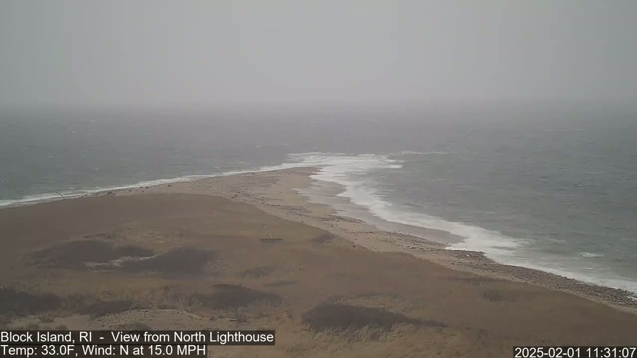 A hazy, overcast day shows a sandy beach curving into a choppy ocean under a gray sky.