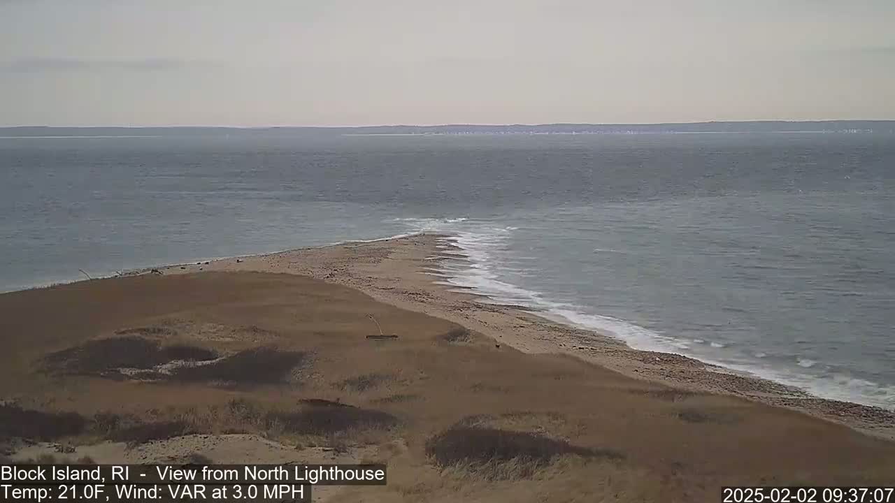 A sandy beach and a narrow strip of land jutting into a gray ocean under an overcast sky.