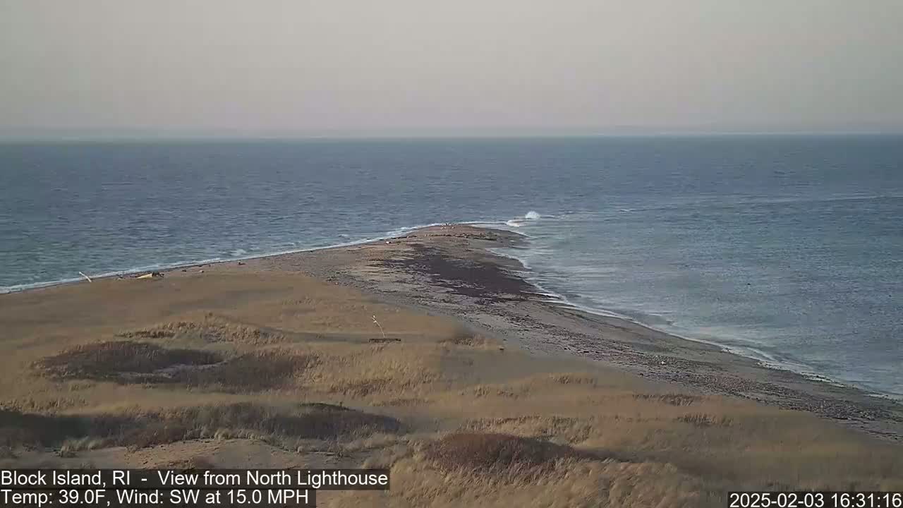 A sandy, dune-covered point of land juts into a somewhat choppy ocean under a gray sky.