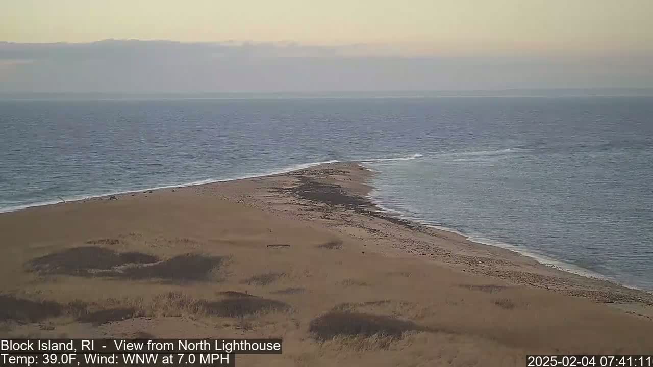 A sandy point of land juts into a calm, gray-blue ocean under a pale, overcast sky.