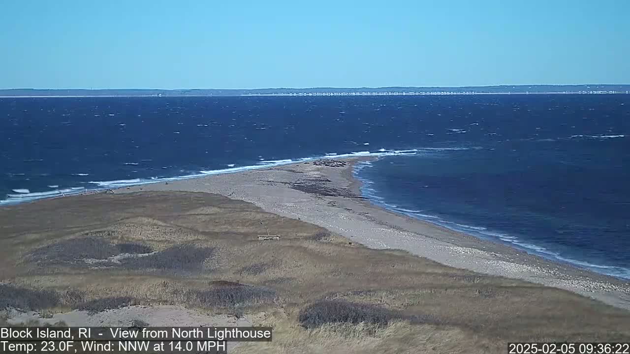 A sandy, grassy point of land juts into a choppy blue ocean under a clear sky.