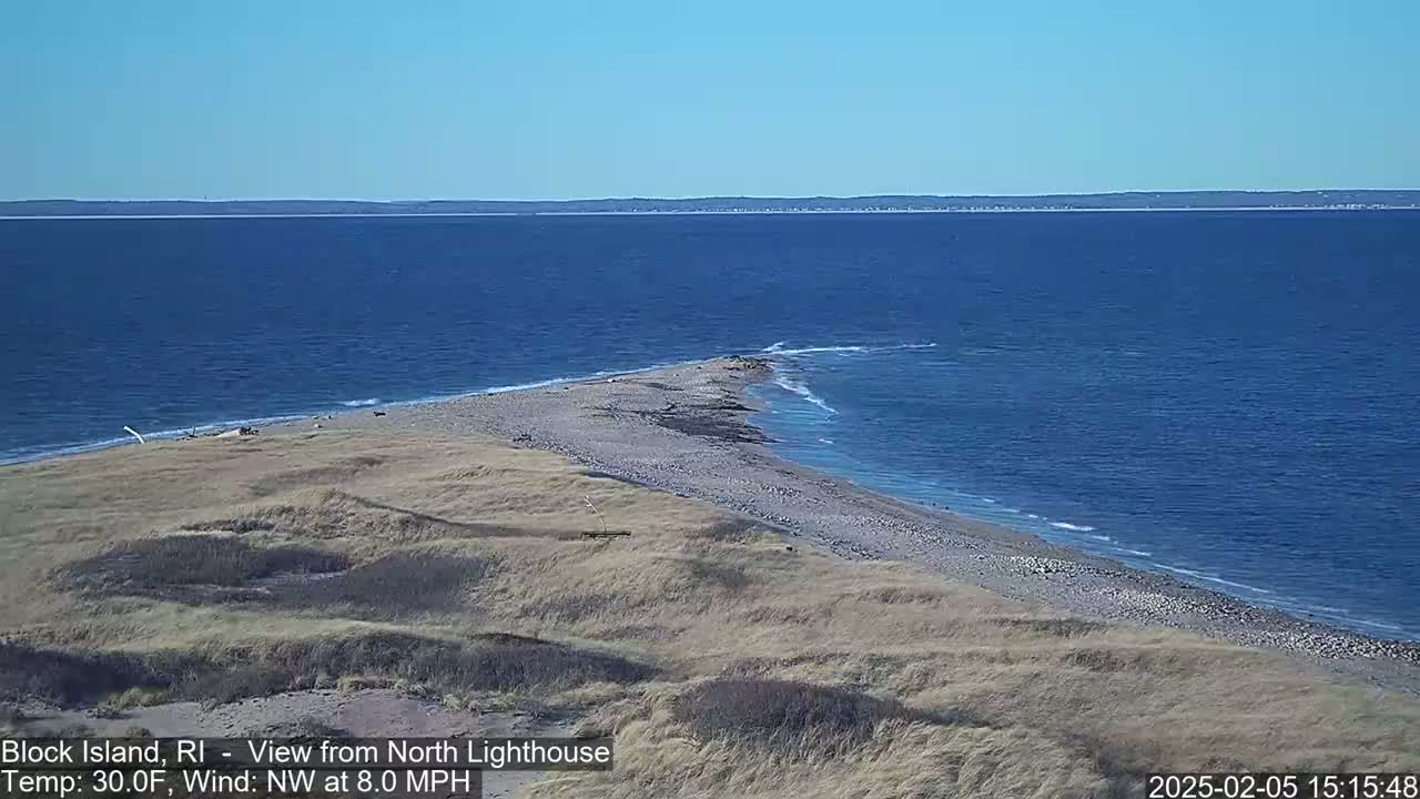 A sandy, curving shoreline extends into a calm, blue ocean under a clear, sunny sky.