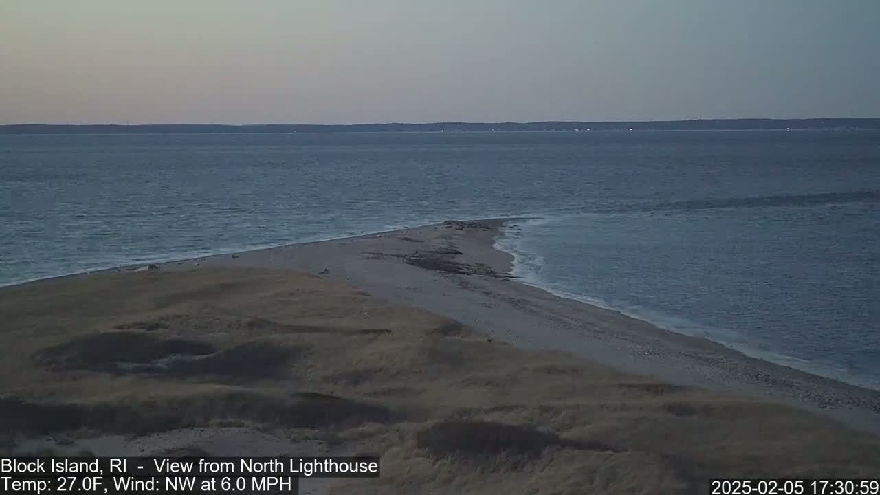 A sandy point of land juts into a calm, dark-blue ocean under a twilight sky.