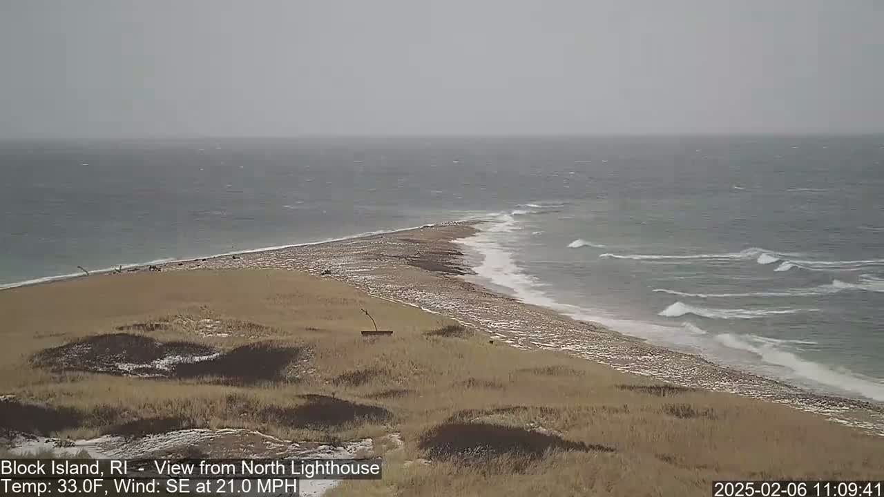 A sandy, snow-dusted peninsula juts into a choppy, gray sea under an overcast sky.