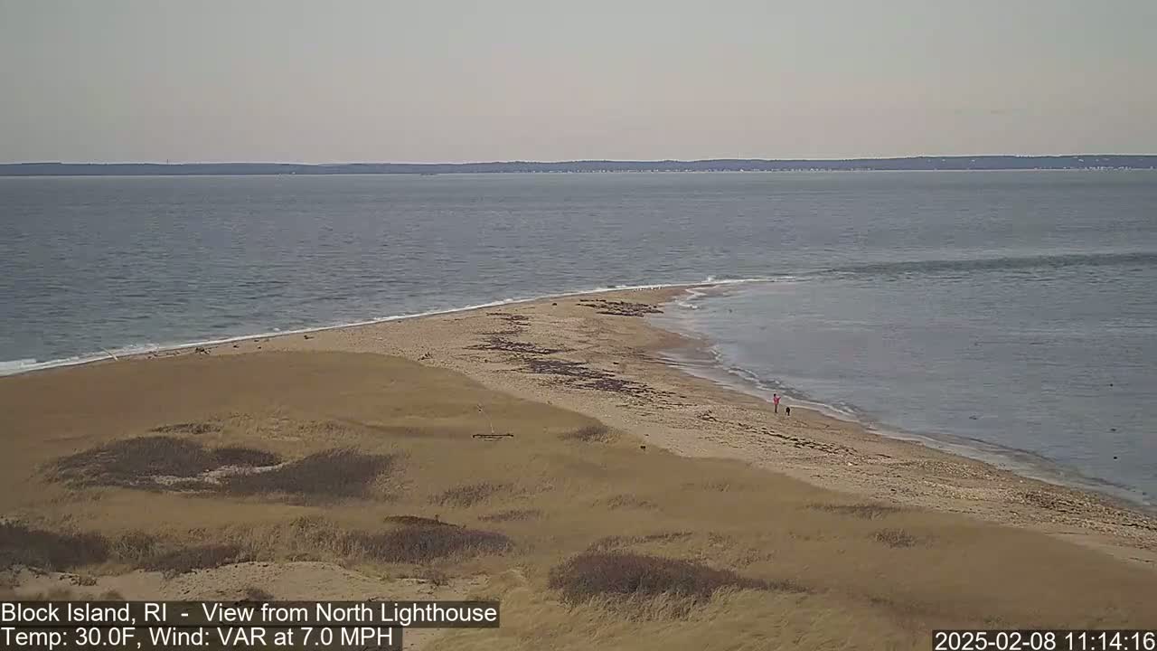 A sandy beach with a few people and a calm ocean under an overcast sky.
