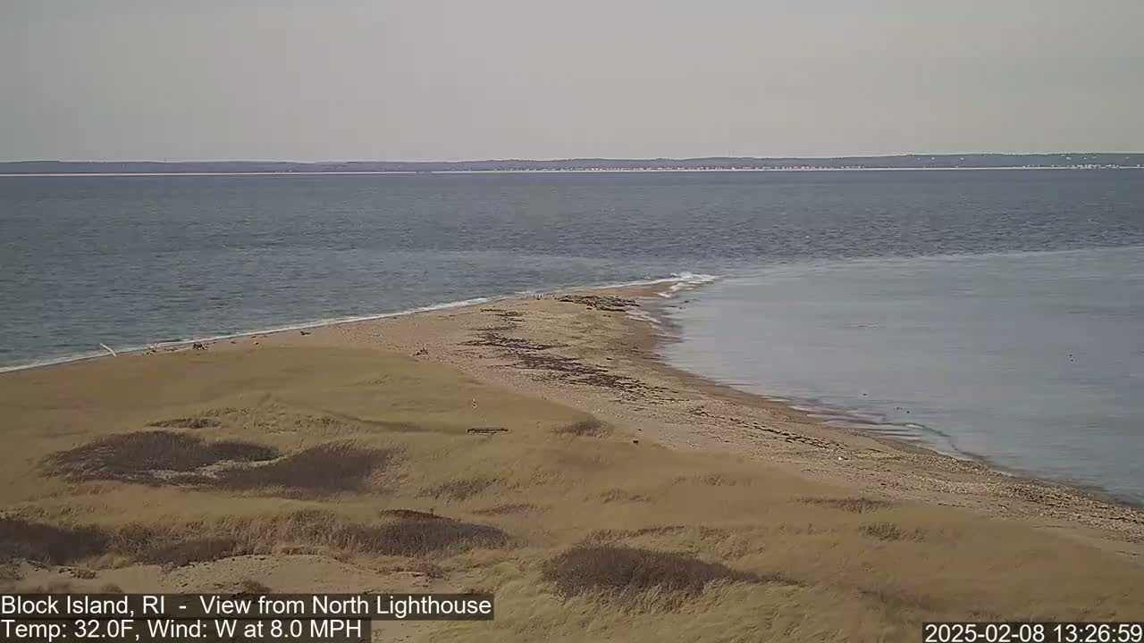 A sandy point of land juts into a calm, gray ocean under a clear, pale sky.