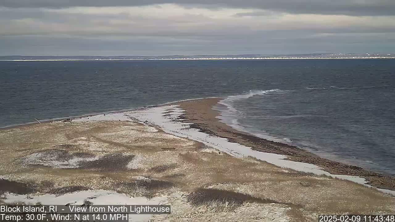 A partly snowy beach and a choppy ocean under a cloudy sky are visible from a high vantage point.