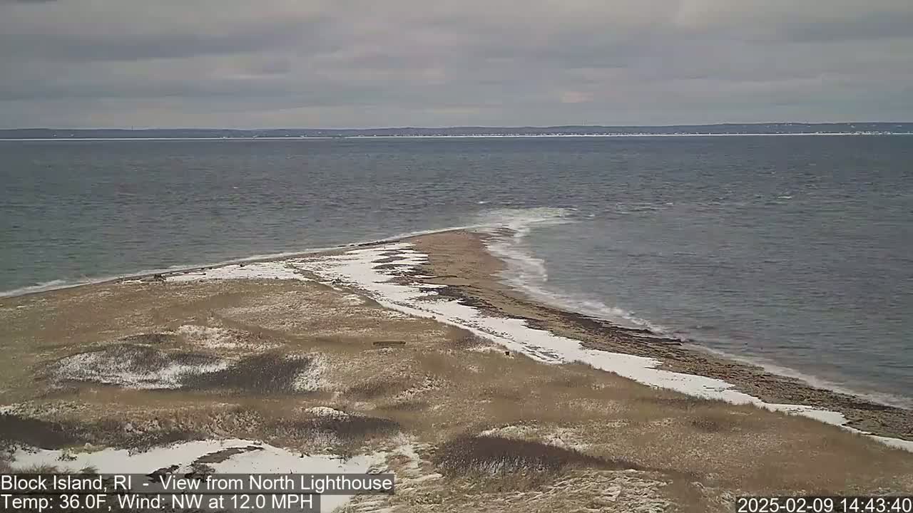 A snow-dusted beach and dune landscape meets a choppy ocean under a cloudy sky.