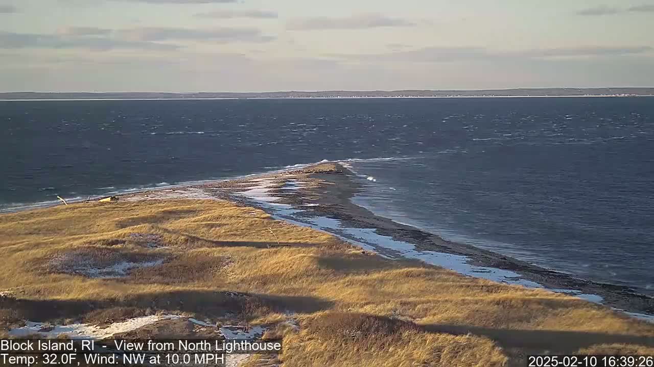 A windy, 32-degree day reveals a coastal scene of tan grasses dusted with snow overlooking a rocky point jutting into a choppy sea.