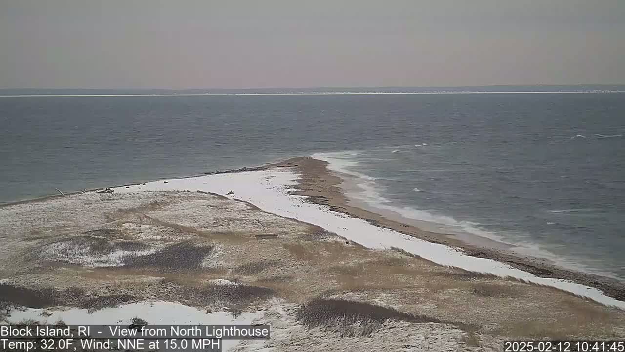 A snow-dusted beach and grassy dunes meet a choppy sea under a cloudy sky.