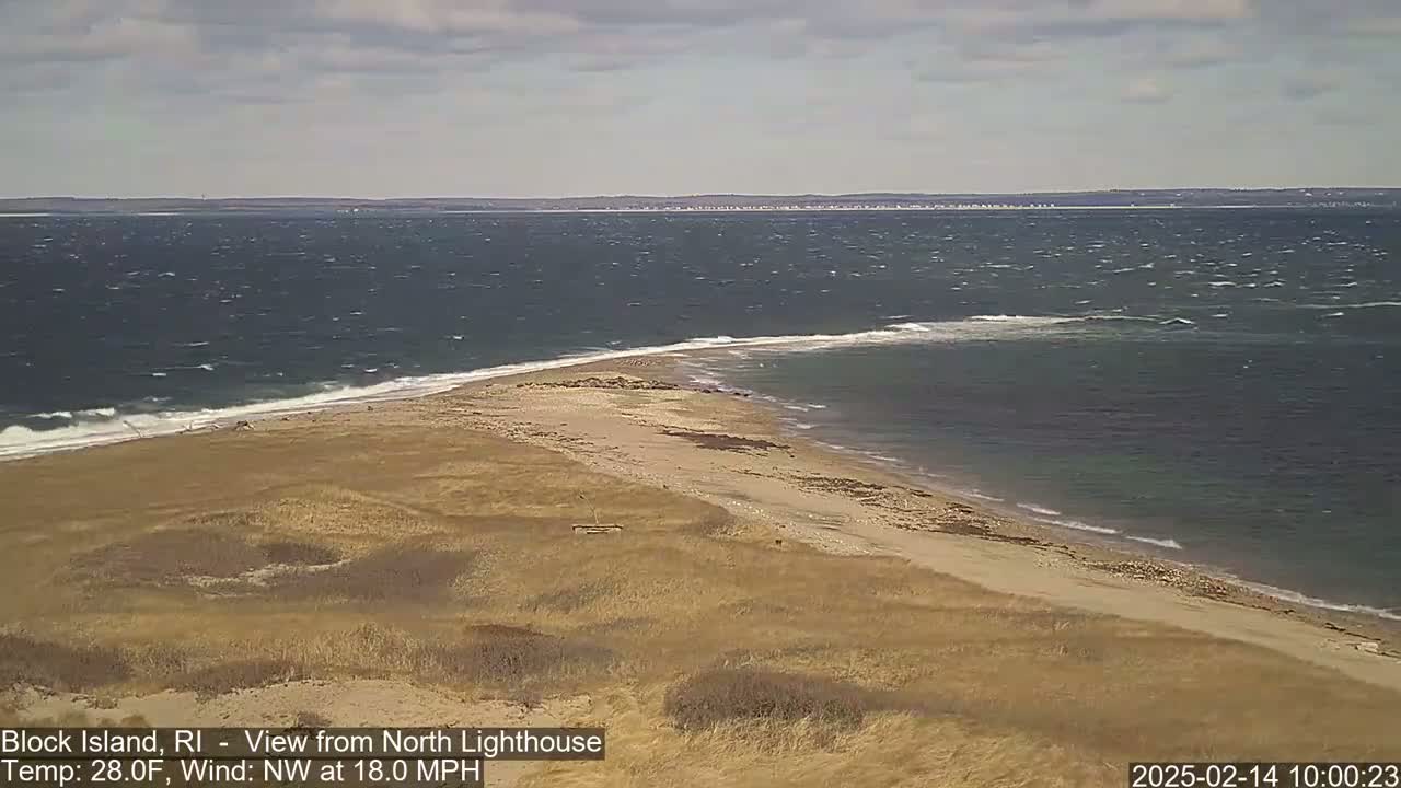 A sandy beach curves into a choppy ocean under a partly cloudy sky with an 18 mph northwest wind.