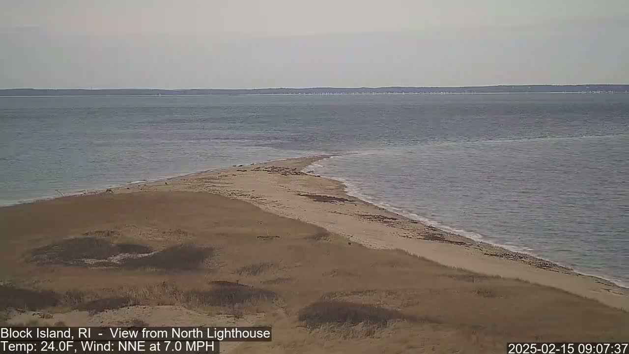 A sandy spit of land juts into a calm, gray ocean under a cloudy sky.