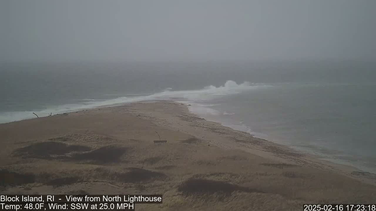 A sandy, dune-covered coastline with crashing waves in overcast conditions.