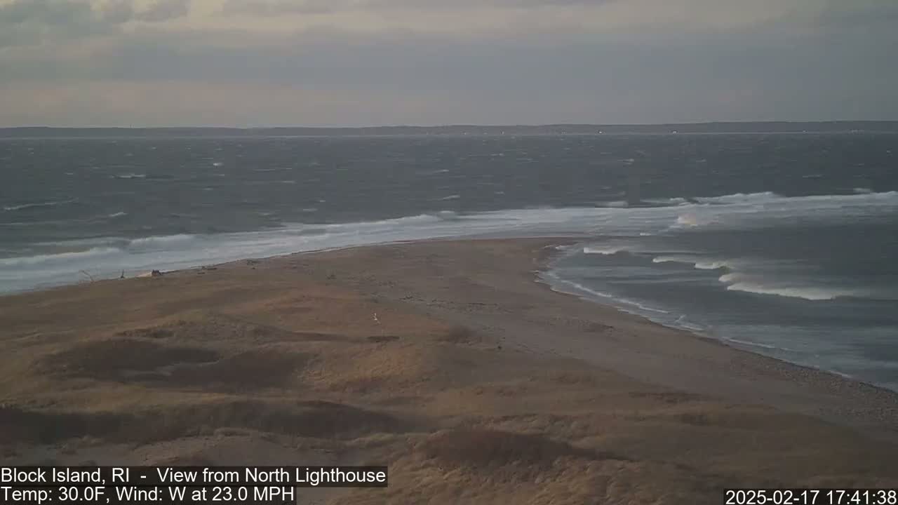 A sandy beach with dunes curves into a choppy ocean under an overcast sky.