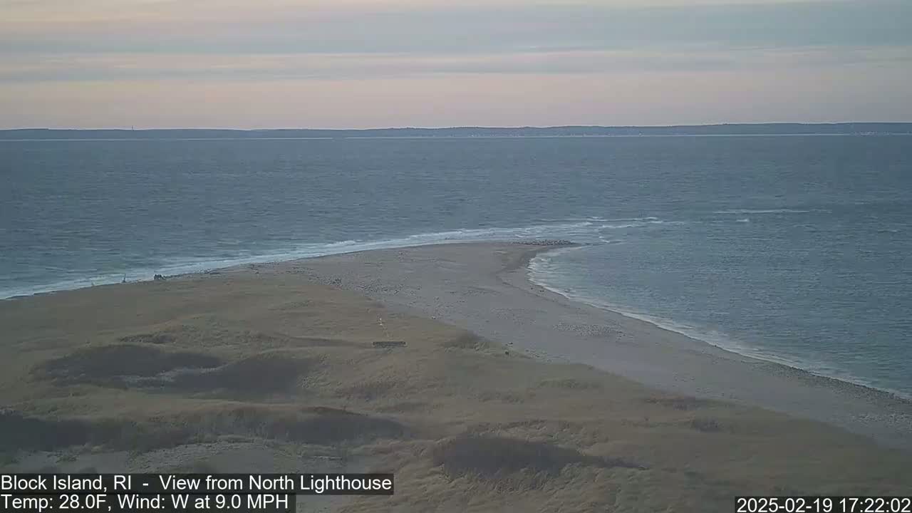 A sandy beach and a narrow spit of land extend into a calm, gray ocean under a pale sky.
