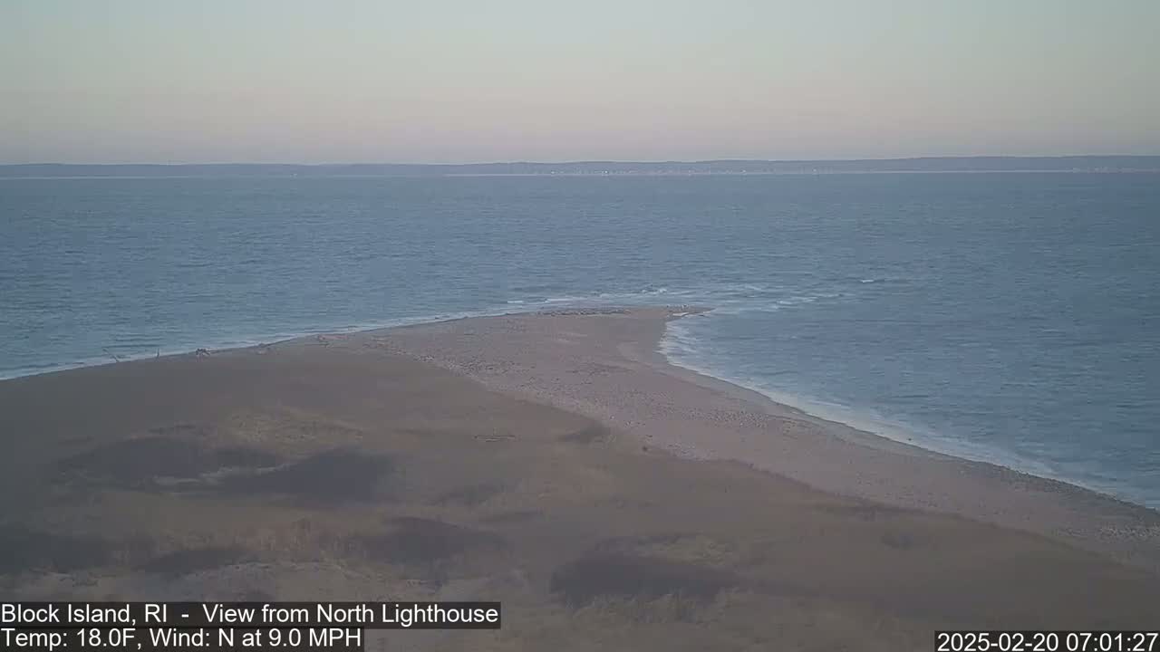 A sandy beach and a calm ocean are visible under a clear, pale sky.