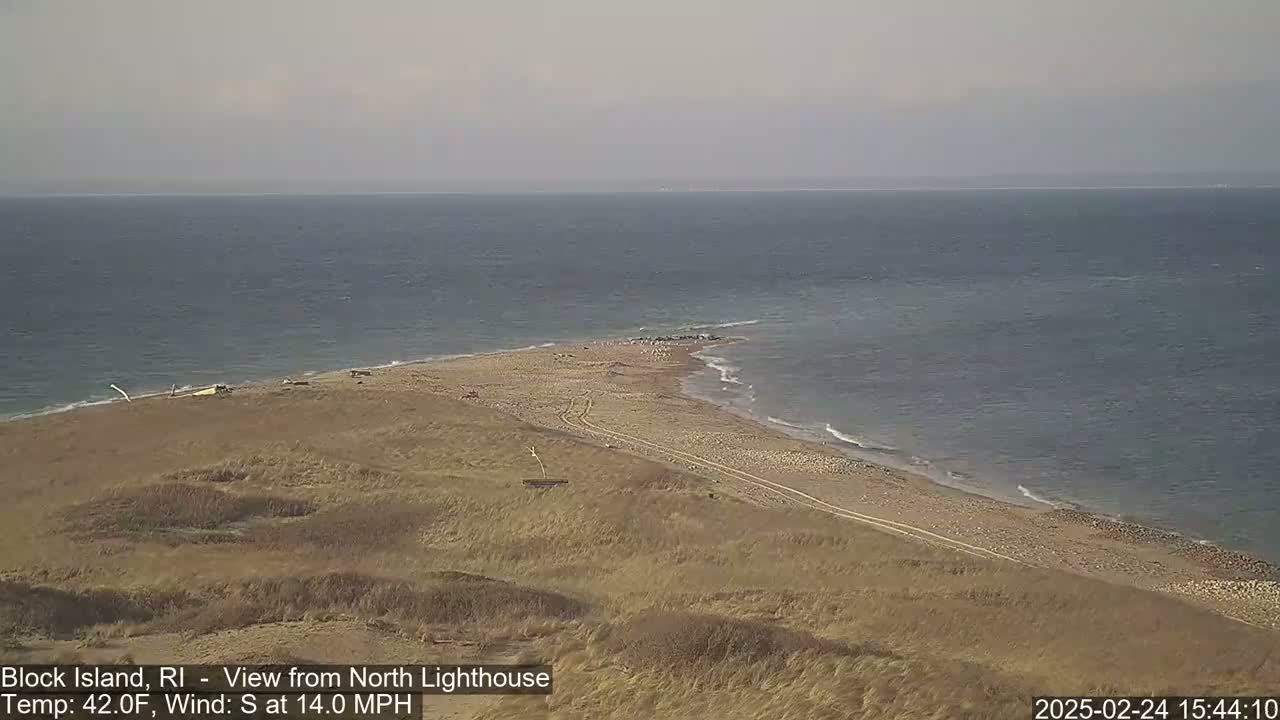 A sandy beach curves into a calm ocean under a hazy sky.