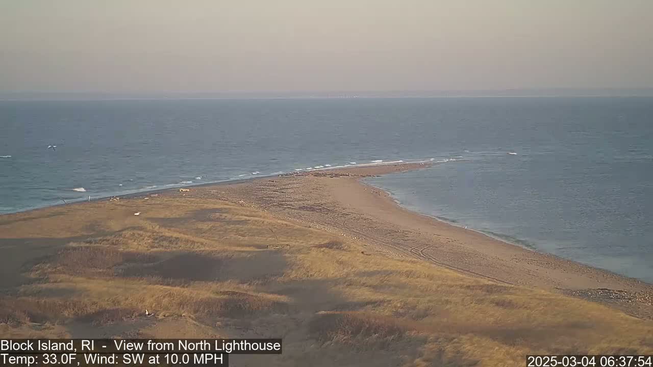 A sandy peninsula juts into a calm sea under a hazy sky.