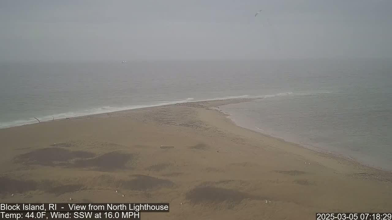 A hazy, sandy peninsula juts into a calm, gray ocean under an overcast sky.