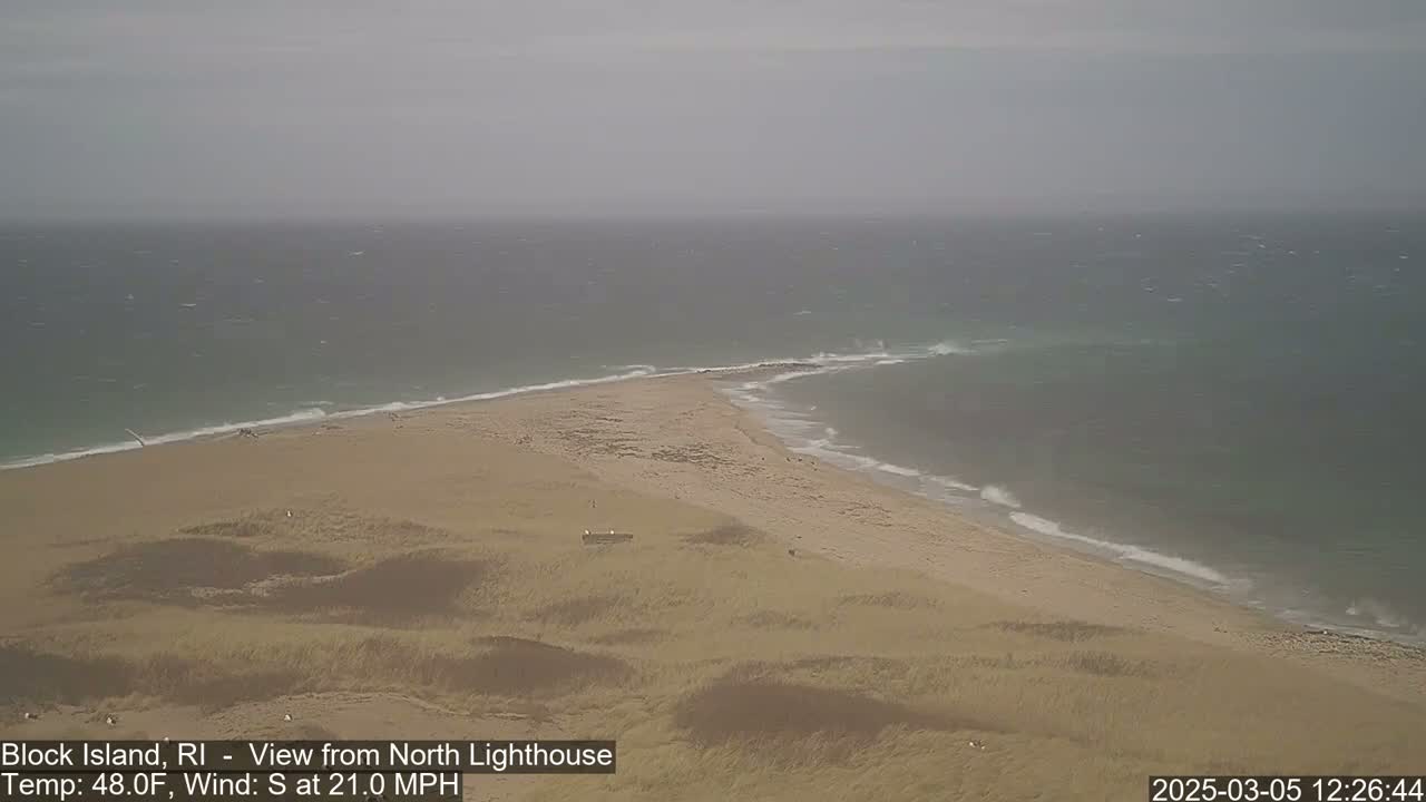 A sandy beach and coastline with a windy, overcast sky and choppy ocean waves are visible from a high vantage point.