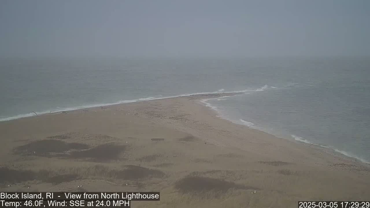 A hazy, sandy spit of land juts into a choppy sea under a gray sky, with a 24 mph wind blowing from the south-southeast.