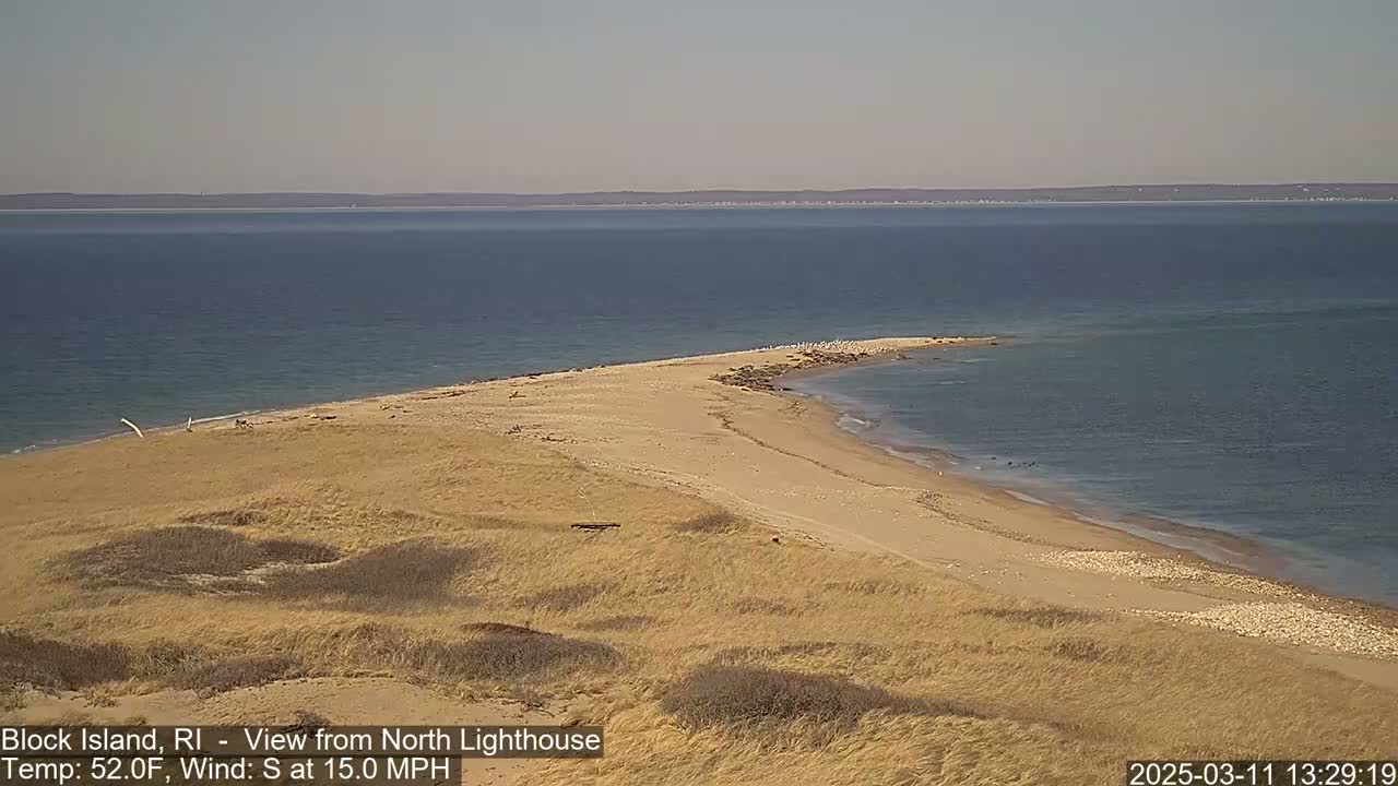 A sandy, curved shoreline juts into a calm, blue ocean under a clear sky.