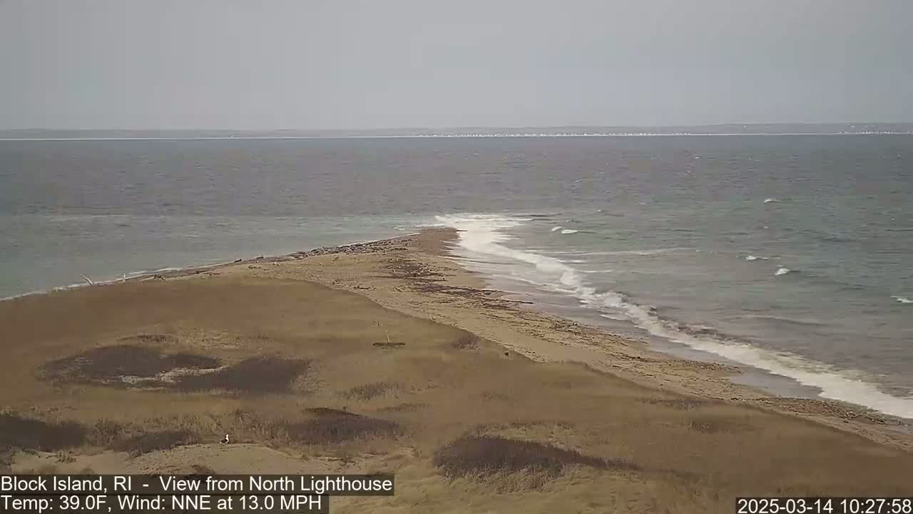 A sandy, dune-covered peninsula extends into a gray, choppy ocean under an overcast sky.