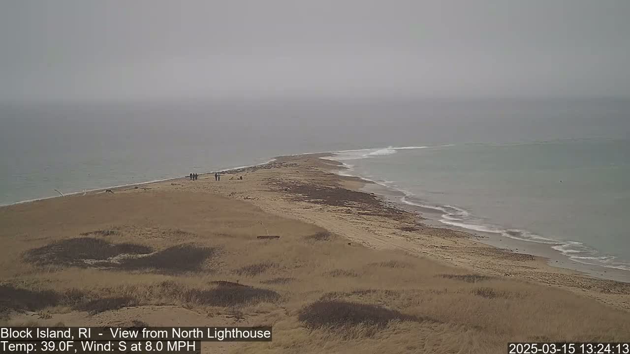 A sandy beach and a narrow spit of land extend into a calm, gray ocean under an overcast sky.
