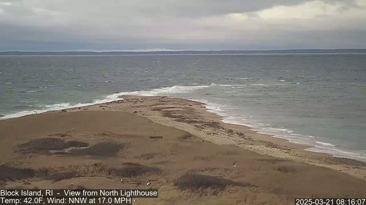 A sandy beach and a point of land jut into a choppy sea under an overcast sky.