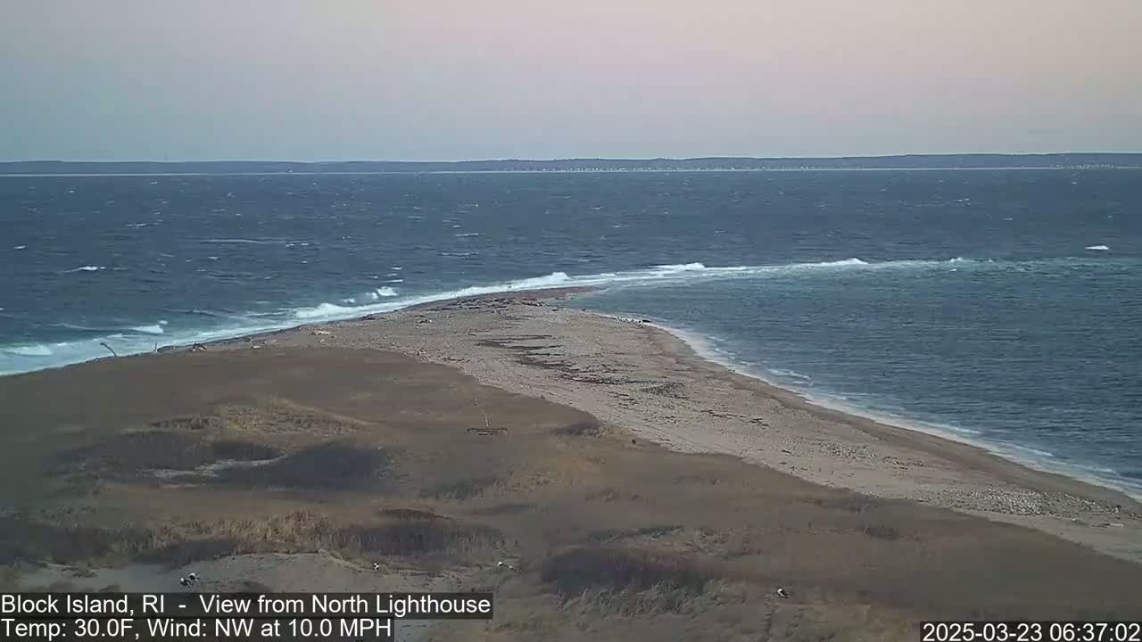 A sandy beach curves into a choppy ocean under a cloudy sky.