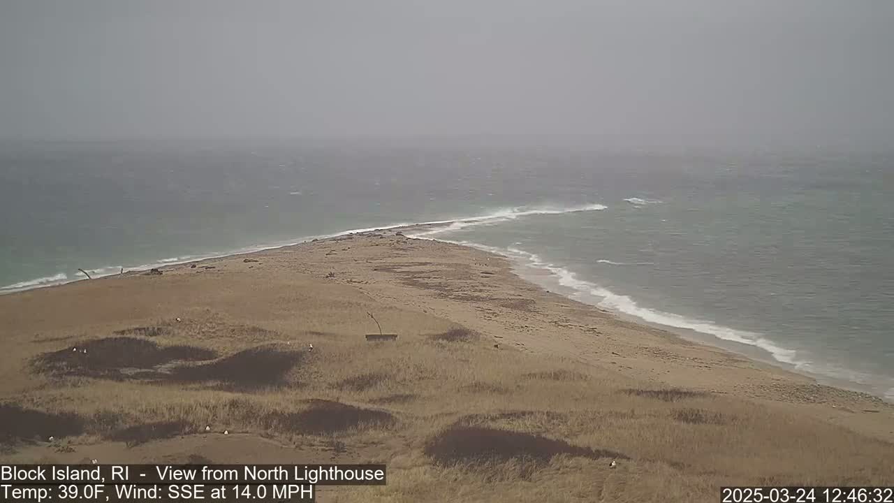 A sandy, grassy point of land juts into a choppy sea under an overcast sky.