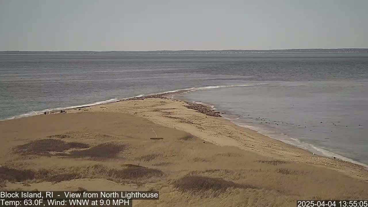 A sandy beach and a calm ocean meet at a point of land under a clear sky.