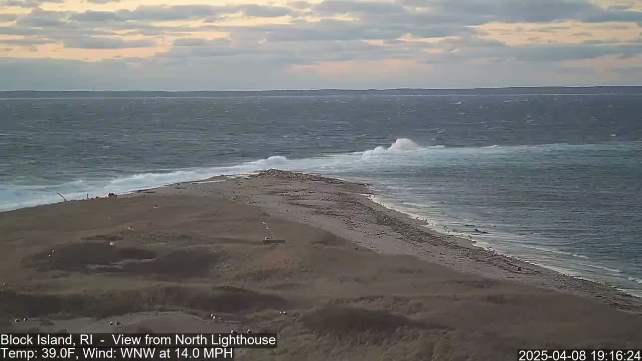 A sandy shoreline with waves crashing against it under a cloudy sky.