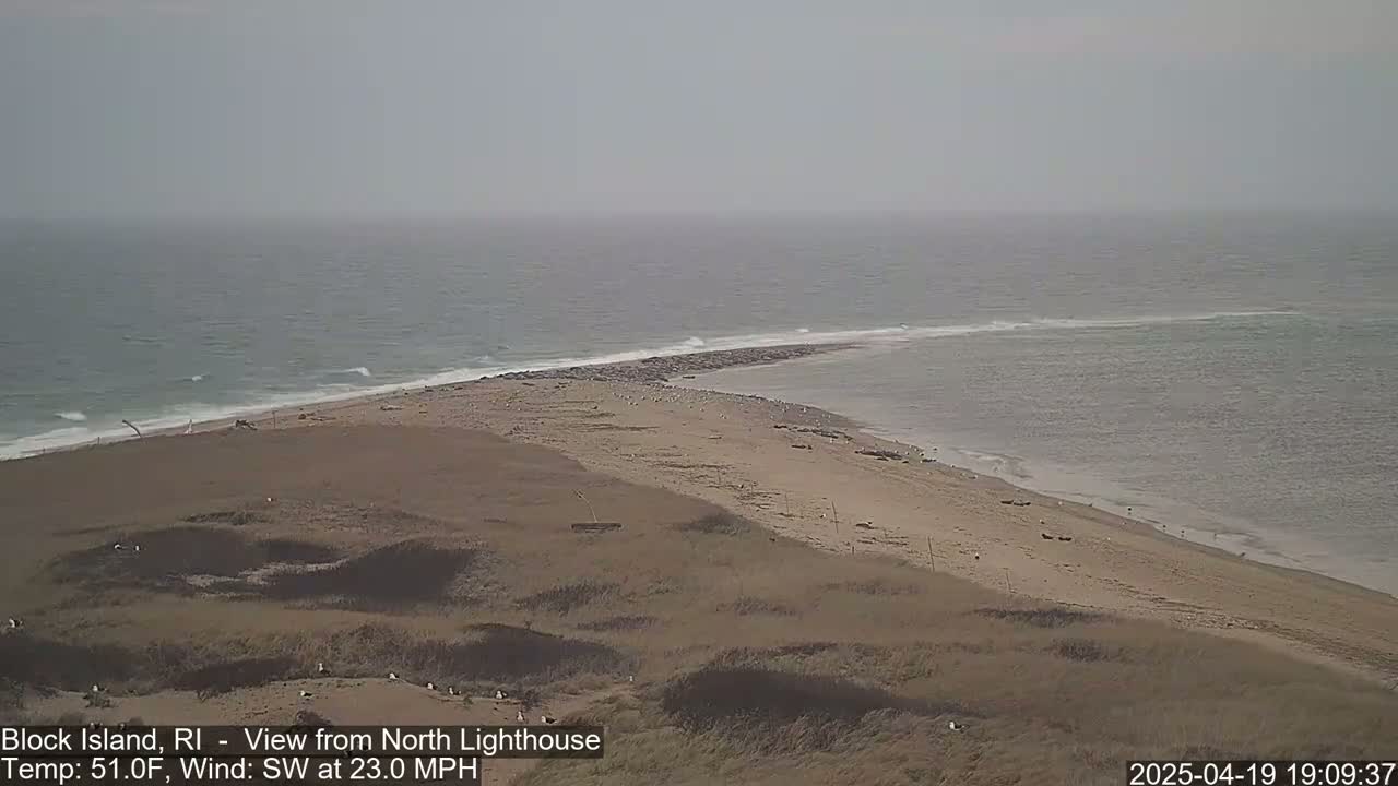 A sandy beach and a narrow strip of land jutting into a calm, gray ocean under an overcast sky.