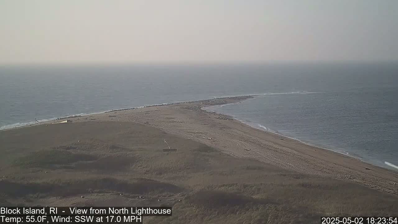 A sandy beach and a narrow spit of land jut into a hazy, gray ocean under a partly cloudy sky.
