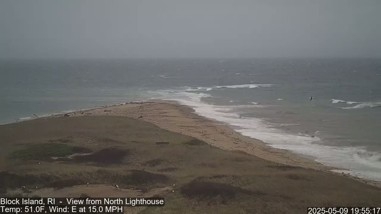 A sandy beach and grassy dunes meet a choppy sea under an overcast sky with a 15 mph east wind.