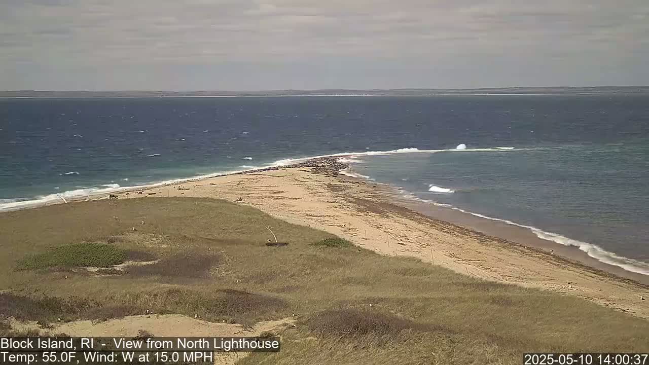 A sandy beach and a point of land jut into a choppy sea under a cloudy sky.